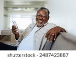 Cheerful man enjoying modern technology at home, sitting comfortably on the couch and smiling joyfully while holding a smartphone