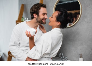 cheerful man with face cream on nose looking at girlfriend with container - Powered by Shutterstock