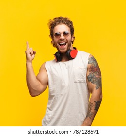 Cheerful man with headphones standing on yellow background and pointing up with index finger.