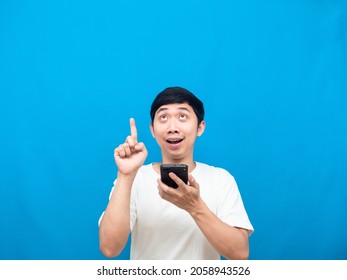 Cheerful Man Holding Cellphone And Point Finger Up At Copy Space Blue Background