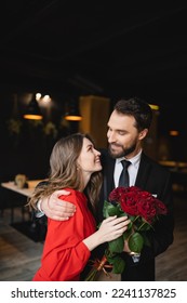 cheerful man hugging happy girlfriend with bouquet of red roses on valentines day - Shutterstock ID 2241137825