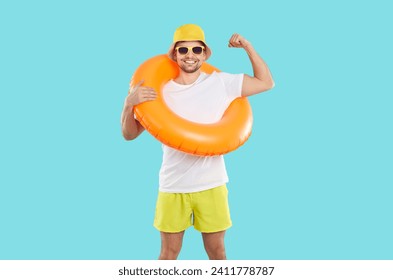 Cheerful man with inflatable swimming circle shows biceps on light blue background. Smiling male vacationer, humorous strong swimmer or beach lifeguard in T-shirt, shorts, panama and sunglasses. - Powered by Shutterstock