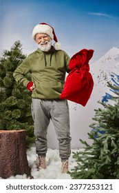 cheerful man in khaki hoodie holding Santa bag and wearing christmassy hat, Merry Christmas