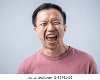 A cheerful man in a pink shirt laughs heartily, his eyes closed and mouth wide open, exuding joy. The background is a plain, light blue backdrop, highlighting his vibrant expression - Powered by Shutterstock