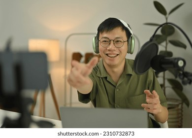 Cheerful man radio host in headphone using condenser microphone to recording podcast in small home studio - Shutterstock ID 2310732873