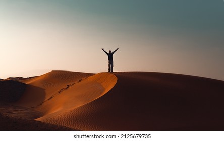 Cheerful Man with Raised Up Hands Enjoying Beautiful Sunset on the Hill of a Desert. Happy Summer Holidays. Active Lifestyle.