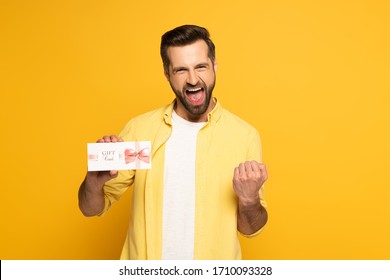 Cheerful Man Showing Yeah Gesture And Holding Gift Card On Yellow Background