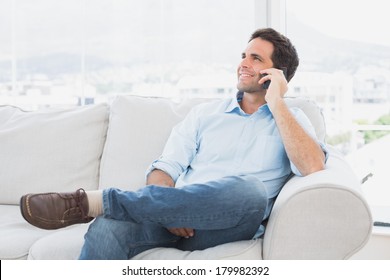 Cheerful Man Sitting On The Couch Making A Phone Call At Home In The Living Room