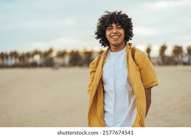 Cheerful man standing on a sandy beach with palm trees in the background, embracing a relaxed and joyful atmosphere under a blue sky.