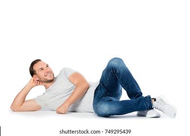 Cheerful man supporting his head on the hand, laying on the floor and looking up. Wandering happy thoughts. Isolated on white background.