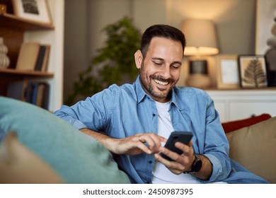 A cheerful man texting his friends and arranging a meet up location while sitting on a couch in his living room. - Powered by Shutterstock