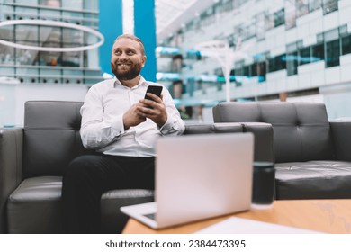 Cheerful man using smartphone while resting on sofa