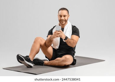 Cheerful man using a smartphone while sitting on a fitness mat in an exercise studio setting, nice app