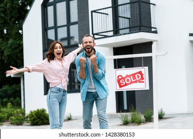 Cheerful Man And Woman Celebrating Near House And Board With Sold Letters 