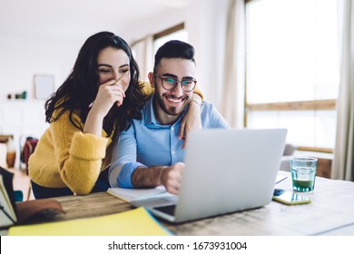 Cheerful man and woman with pencil in had near face smiling while planning further work together and using laptop at home 