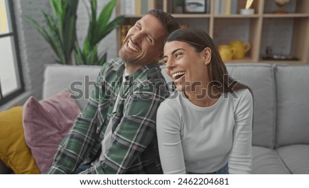 A cheerful man and woman sit closely on a sofa, laughing heartily in a cozy, well-decorated living room.