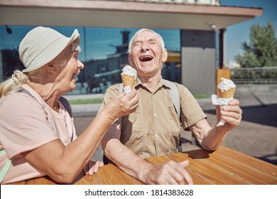 Cheerful Married Elderly Couple With Vanilla Ice Cream Waffle Cones Laughing Heartily At The Table