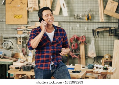 Cheerful mature Asian carpentry shop owner talking on phone with client - Powered by Shutterstock