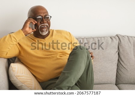 Cheerful Mature Black Man Chatting On Cellphone Having Pleasant Phone Call Sitting On Couch At Home. Senior Male Having Mobile Conversation Via Smartphone Looking Aside. Communication Concept Stock foto © 