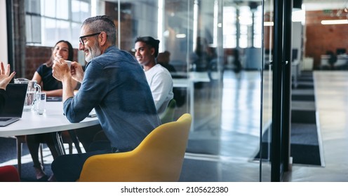 Cheerful mature businessman attending a meeting with his colleagues in an office. Experienced businessman smiling while sitting with his team in a meeting room. Creative businesspeople working together