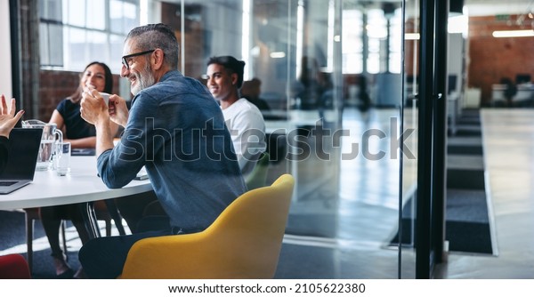 Cheerful mature businessman attending a meeting\
with his colleagues in an office. Experienced businessman smiling\
while sitting with his team in a meeting room. Creative\
businesspeople working\
together