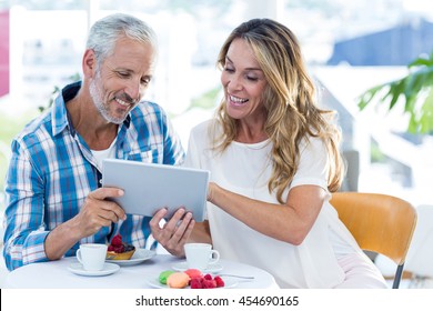 Cheerful Mature Couple Looking In Digital Tablet While Sitting By Table At Restaurant