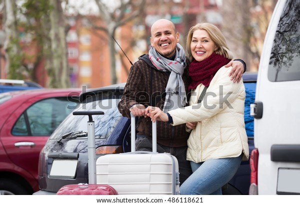 Cheerful mature couple with luggage standing at\
street and smiling. Focus on\
man\
