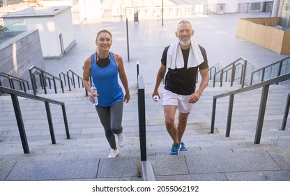 Cheerful Mature Couple, Man And Woman In Sportswear Smiling At Camera, Walking Up The Stairs After Working Out Together Outdoors