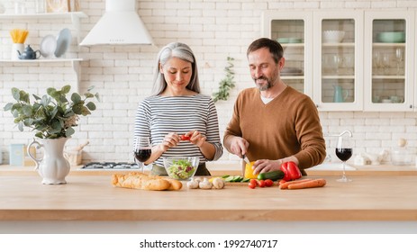 Cheerful Mature Couple Middle-aged Family Wife And Husband Cooking Vegetable Vegetarian Salad Together In The Kitchen At Home. Parents Preparing Meal Food For Romantic Dinner