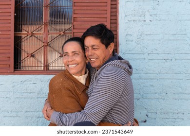 Cheerful Mature couplestanding and embracing each other outside the house. Togetherness, multi-generation family, support concept.