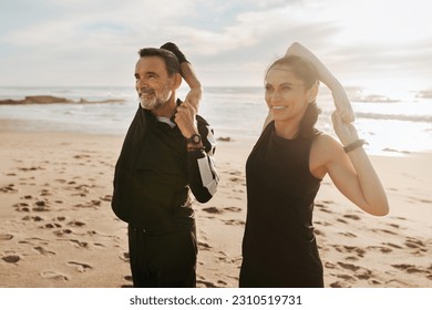 Cheerful mature european man and lady doing arm exercises, stretching and warmup, enjoy workout together on sea beach. Sports outdoor, fitness and body care in morning, health care - Shutterstock ID 2310519731