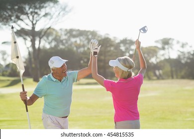 Cheerful mature golfer couple giving high five while standing on field - Powered by Shutterstock