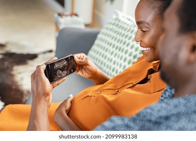 Cheerful Mature Pregnant Couple Watching Ultrasound Picture On Mobile Phone. Smiling Middle Aged Black Pregnant Woman With Husband Feeling Happy And Excited On Seeing Baby Ultrasound On Smartphone.