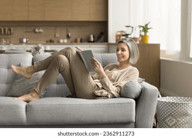 Cheerful mature reader enjoying bestseller, leisure, relaxation, home education, reading paper book in white empty cover, resting on couch, laughing, having fun, studying, doing homework - Powered by Shutterstock