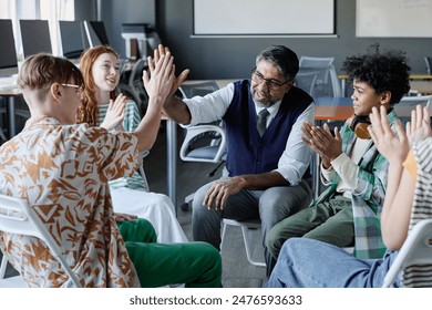 Cheerful mature school psychologist doing high five with male student during group therapy session, other teenagers clapping hands - Powered by Shutterstock