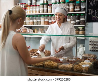 Cheerful Mature Shop Woman Offering Client Nuts And Smiling 