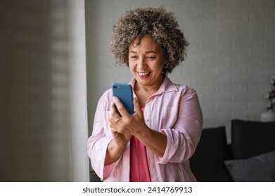 A cheerful mature woman is actively sending and receiving messages on her smartphone, spreading positive vibes - Powered by Shutterstock