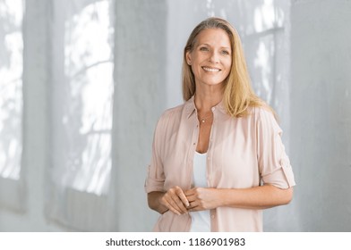 Cheerful mature woman in casual looking away indoor. Successful senior woman smiling and standing confidently. Portrait of happy beautiful lady in a pink shirt with toothy smile standing. - Powered by Shutterstock