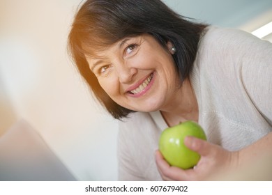 Cheerful Mature Woman Eating Green Apple