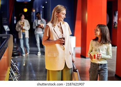 Cheerful Mature Woman And Her Daughter Holding Fizzy Drink And Bucket Of Popcorn Going To Watch Movie At Cinema