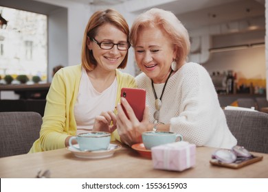 Cheerful mature woman and her lovely senior mother browsing online together, using smart phone - Powered by Shutterstock