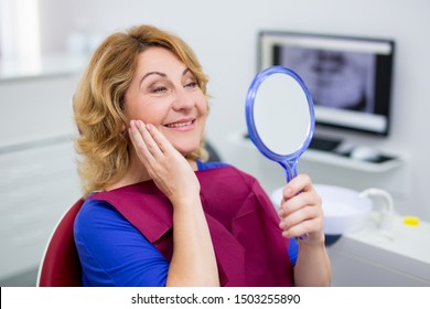 Cheerful Mature Woman Looking At Her Teeth In Dental Clinic