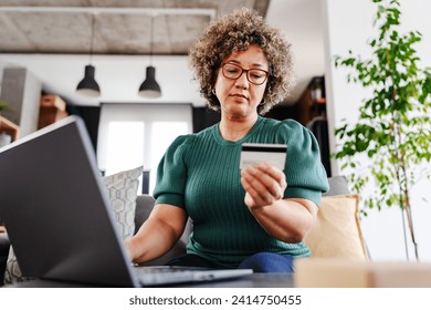 A cheerful mature woman is making an online purchase or payment, utilizing a credit card and a laptop computer. Online banking concept - Powered by Shutterstock