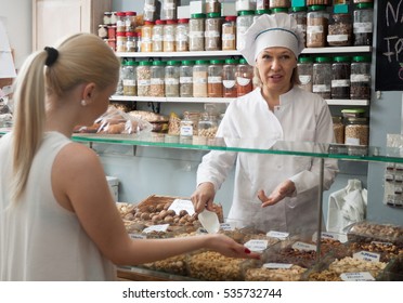 Cheerful  Mature Woman Offering Client Different Nuts In Local Supermarket