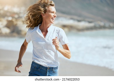 Cheerful mature woman running on the beach on a sunny day. Beautiful middle aged woman laughing, being active and having fun during summer vacation. Energetic lady spending her free time by the sea - Powered by Shutterstock