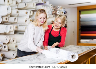 Cheerful Mature Woman Seller Displaying Diverse Fabrics To Young Customer In Textile Shop