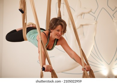 Cheerful Mature Woman Smiling, Doing Superman Pose On Fly Yoga Hammock