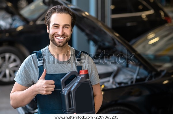 Cheerful mechanic approving of the engine oil\
before the camera