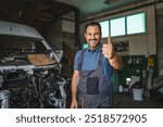 A cheerful mechanic in overalls smiles confidently, giving a thumbs up in a workshop, conveying satisfaction and readiness to assist with any car repairs.