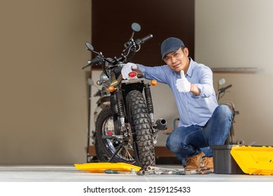 Cheerful mechanic repairing motorcycle in workshop garage, Smiling man fixing motorbike in repair shop, Man showing thumbs up, Repairing and maintenance concepts - Powered by Shutterstock